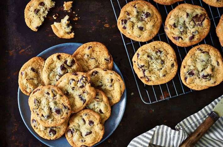 a plate with chocolate chip cookies next to a cooling rack with more cookies