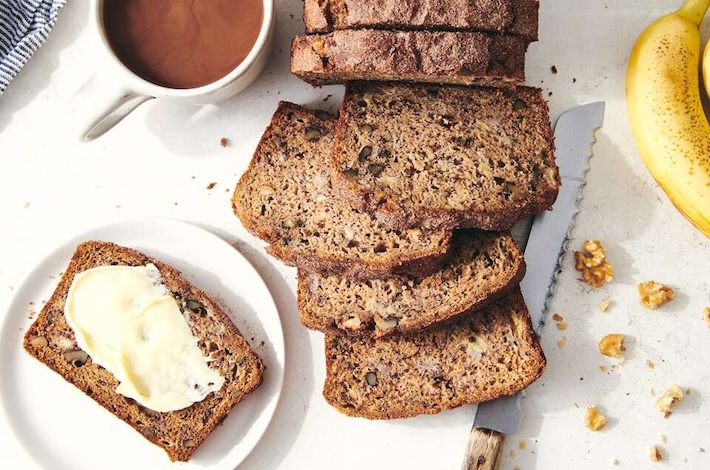 sliced loaf of banana bread next to a buttered slice on a plate and a mug of coffee